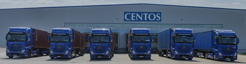 Bild mit einem Menschen, der einen Hubwagen mit einem Karton durch eine Lagerhalle schiebt